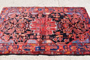 A Middle Eastern red ground wool rug, hand woven in deep pile, the centre depicting stylized figures