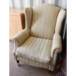 A modern wingback armchair upholstered in cream with gold bands.