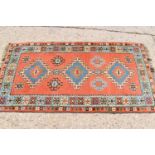 A Persian wool rug with orange ground, triple diamonds to the center and stylized borders, 198cm