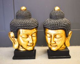 A pair of 20th century Buddha heads, with gilded faces, raised on square plinths, 56cm high.