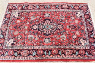 A Persian wool rug with red ground, the central motif bordered by flowers and having a border of