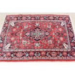 A Persian wool rug with red ground, the central motif bordered by flowers and having a border of