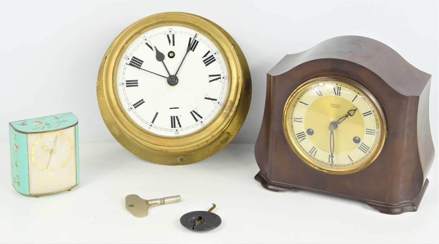 A brass circular bulkhead clock, a Bakelite Smiths clock and a small painted Kienzle clock.