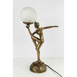 An Art Deco style table lamp in the form of a dancing lady holding opaque glass shade in her hand,