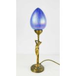 An Art Nouveau style brass table lamp in the form of a nude female, and having an iridescent glass