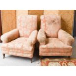 A pair of antique Howard style upholstered armchairs with deep set seats, raised on short mahogany