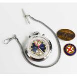A pocket watch with visible mechanism, together chain and two badges.