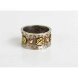 A silver and gold handmade ring with a hammered finish and bearing spiral and dot design in gold,