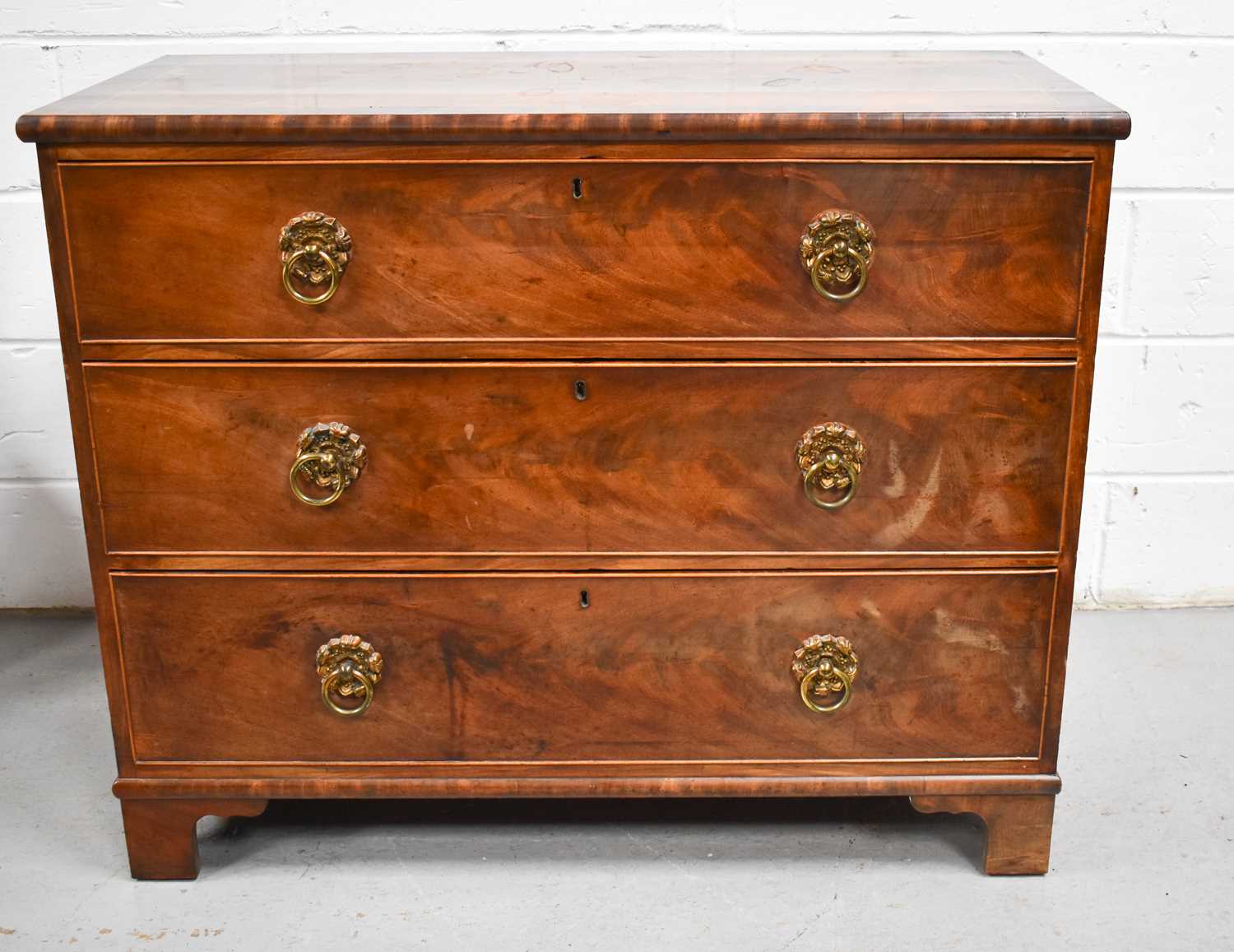 A George III mahogany chest of drawers, the rectangular top above three long drawers, with lion mask