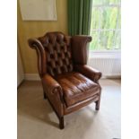 A 20th century wing back armchair, with button back leather upholstery, seat cushion, on block