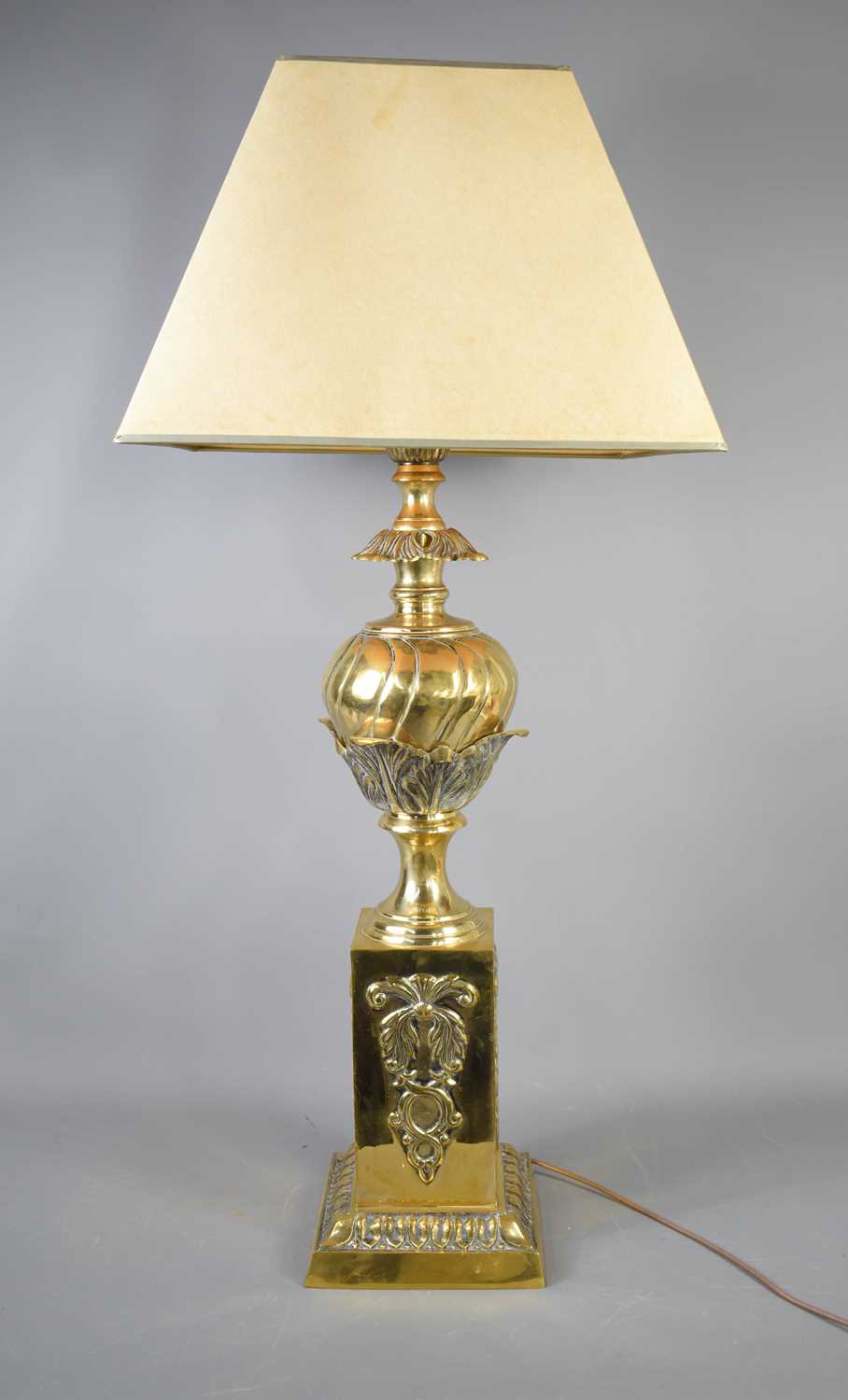 An antique brass lamp base, embossed with decoration, with cream shade, 95cm to the top of shade.