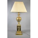 An antique brass lamp base, embossed with decoration, with cream shade, 95cm to the top of shade.