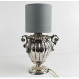 A silver plated lamp base, with three handles, of lobed form with embossed decoration, circa 1900.