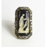 A Victorian white metal and paste mourning ring with an enamelled centre depicting a woman beside