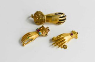 Two gold hand form clasps, set with gemstones together with a gilt metal example, the gold testing