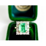 An 18ct yellow gold, emerald and diamond ring, the cushion cut emerald bordered by twelve