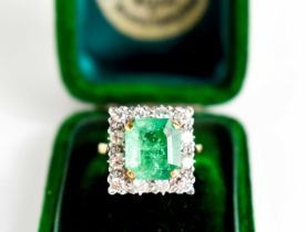 An 18ct yellow gold, emerald and diamond ring, the cushion cut emerald bordered by twelve
