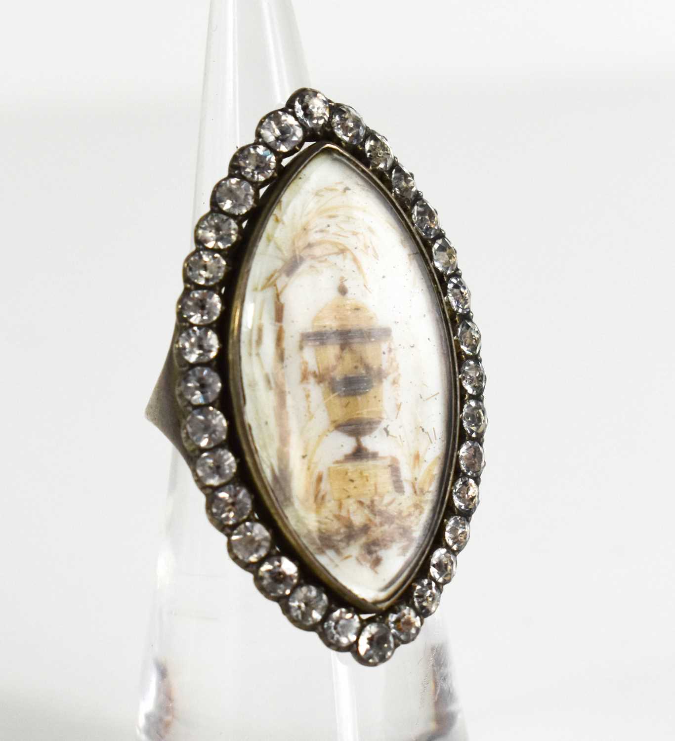 A Victorian white metal and paste mourning ring of marquise form, the enamel centre depicting an urn