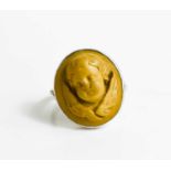 A white metal ring, with relief moulded stone ring in the form of a winged cherub head, size N/O,