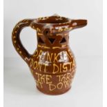 A terracotta slipware glazed puzzle jug, with three spouts, and bearing the inscription 'Drink me up