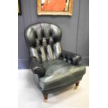 A green leather button back armchair, with turned mahogany legs and brass castors.