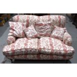 A two seater sofa in the style of Howard and Sons, upholstered in cream and red fabric decorated