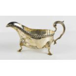 A silver sauce boat, raised on three stepped feet, with a gadrooned edge and decorative foliate