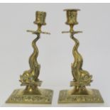 Pair of brass candlesticks with foliate moulded sconces and drip trays on dolphin moulded columns