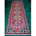 Qashqai hand-knotted runner decorated with four geometric medallions on red ground, 230cm x 136cm.