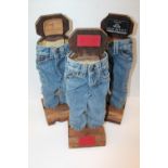 Three pair of decorative miniature denim jeans on wooden stands by Old Rivet and Leon Co, 49cm tall.