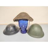 Three British military helmets comprising of a WW2 Brodie helmet with camouflage net, a Home Front