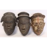 Three African carved wooden masks, probably Nigerian, two with dark staining and one with traces