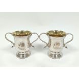 Pair of early Sheffield plated two-handled cups with loop handles, crested, on inset mahogany bases,