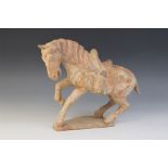 A Chinese pottery model of a horse, possibly Tang dynasty, modelled with one leg raised, with saddle