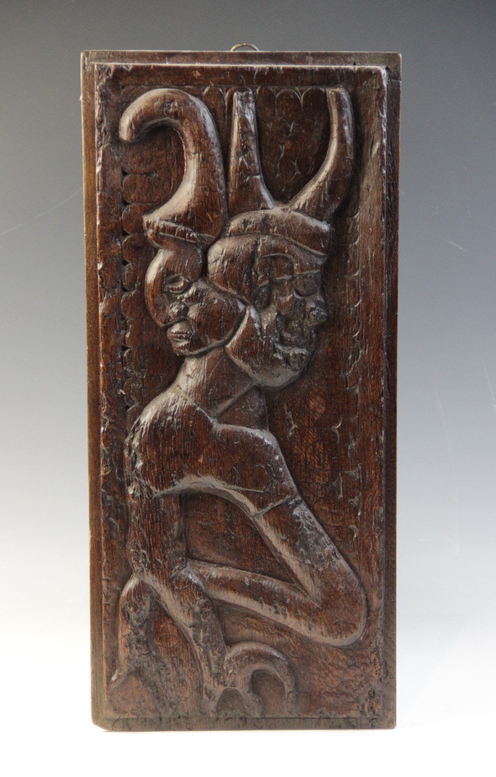 A 16th century carved oak panel, carved with a grotesque beast against a naïve scalloped and foliate