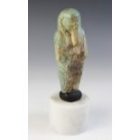A fragmentary Egyptian green glazed faience shabti, holding two hoes with four horizontal bands of