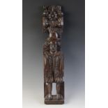 A James I carved oak figural term, carved with a well dressed gentleman modelled standing topped