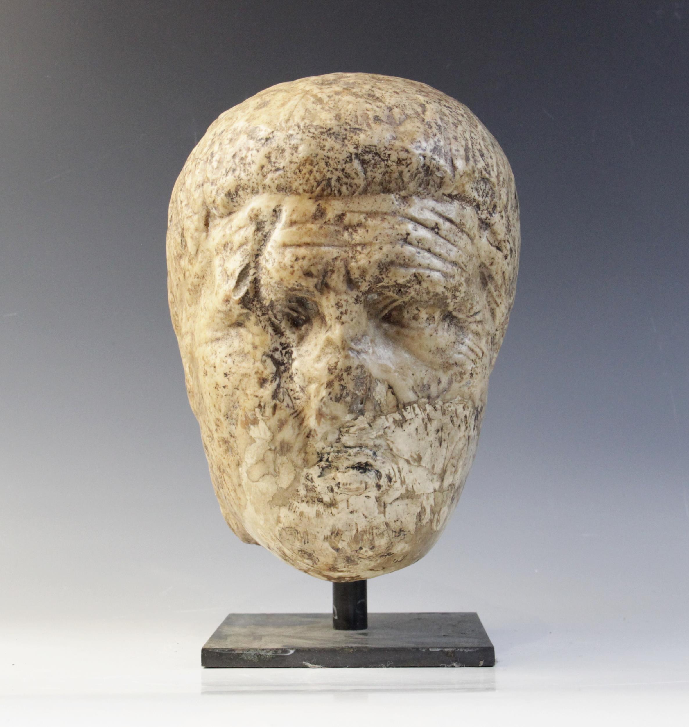 A worn marble male head carved with deeply furrowed brow, with restorations, 26cm high Provenance: