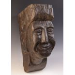 An early 16th century naïve carved oak figural corbel, carved with a smiling face, within a scroll