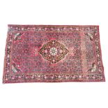 * A Persian pattern wool rug, of traditional design, the central foliate lozenge upon a red ground