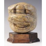 A carved stone sculpture of a grinning grotesque mask, 15.5cm high, mounted upon a rod and hexagonal