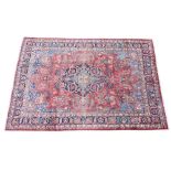 * A Persian pattern wool rug, having a central blue medallion on a red ground, enclosed by foliate