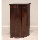 A George III mahogany bow front hanging corner cupboard, the pair of flame mahogany doors opening to