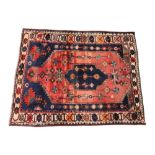 An Iranian wool rug, in red and blue colourways, the central red field inset with a geometric blue