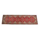 A Caucasian hand knotted wool runner, in red, ivory and blue colourways, the central field with