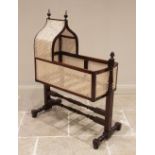 A Victorian mahogany and rattan cradle, the ogee shaped canopy with turned finials above rattan side