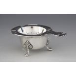 A silver tea strainer and associated stand, the strainer with circular pierced bowl with shaped