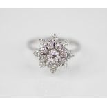 A diamond floral cluster ring, comprising a central round brilliant cut diamond weighing 0.10 - 0.15