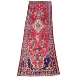 A Persian Sarouk runner, with geometric medallion surrounded by foliate sprays against a red ground,