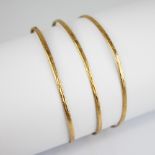 Three gold coloured bangles, each of circular form with engine turned decoration to the exterior,